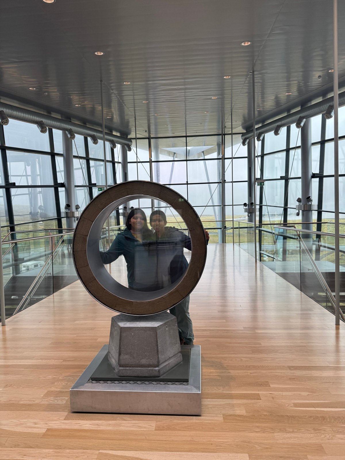 Sufee and her sister posing in a circular sculpture at a glass-walled building in Iceland